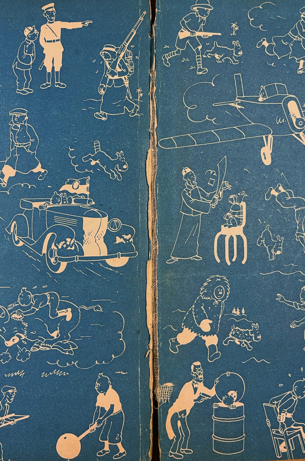 Gardes bleues illustrées d’un album Tintin ancien d’Hergé, présentant une déchirure importante au niveau du fond de cahier et une reliure fragilisée.