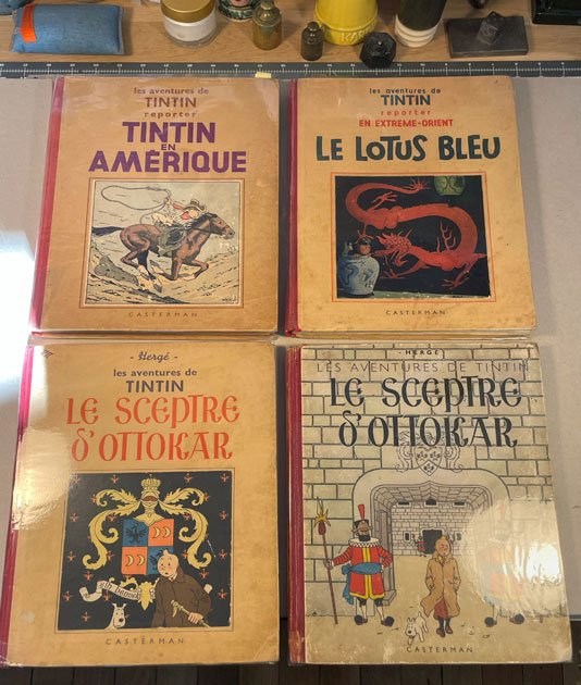 Quatre albums Tintin anciens d’Hergé réunis à l’atelier de restauration : Tintin en Amérique, Le Lotus bleu et deux éditions du Sceptre d’Ottokar, avec leurs cartonnages illustrés d’origine. Titre de l’image