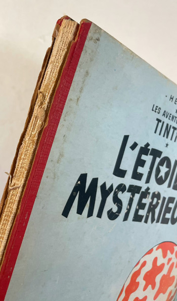 Album Tintin ancien L’Étoile mystérieuse d’Hergé avant restauration : dos manquant, couture apparente et reliure endommagée.