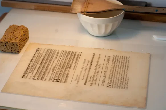 Restauration d’un document graphique avec renforcement du papier à la Tylose et mise en presse pour séchage.